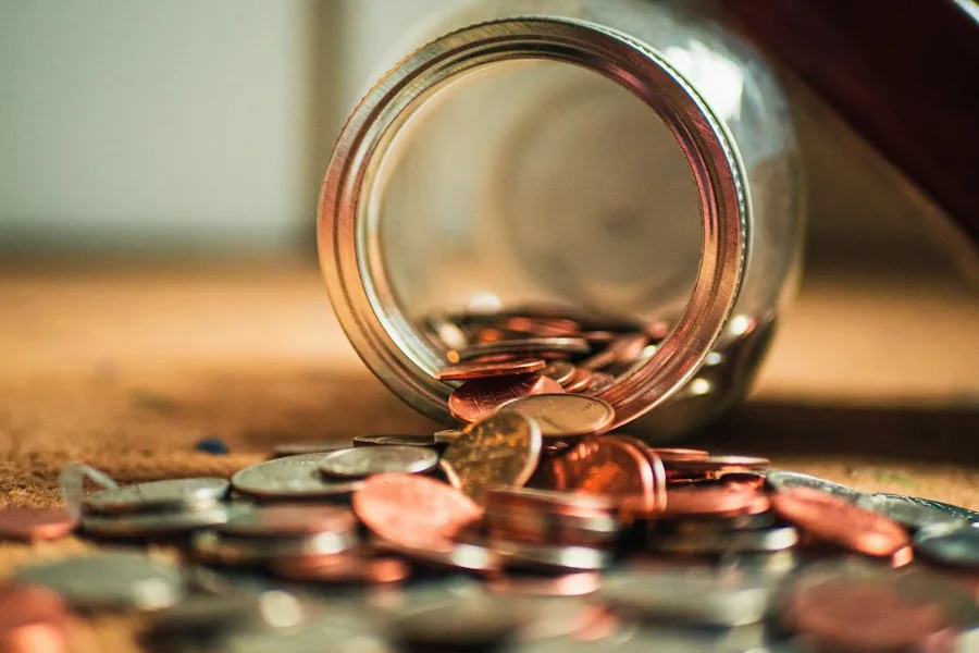 Coins spilling out of a tipped-over glass jar (illustrative stock photo)
