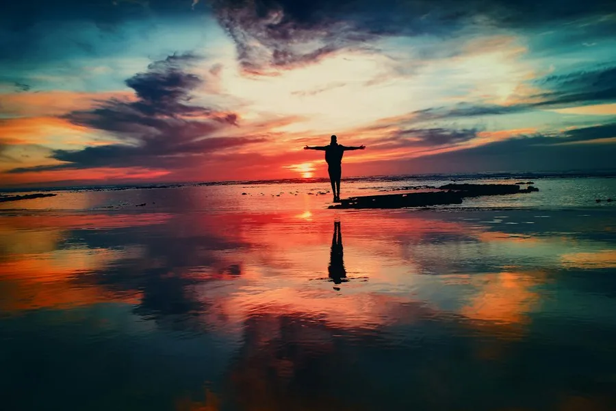 Person standing on reflective water at sunset (illustrative stock photo)