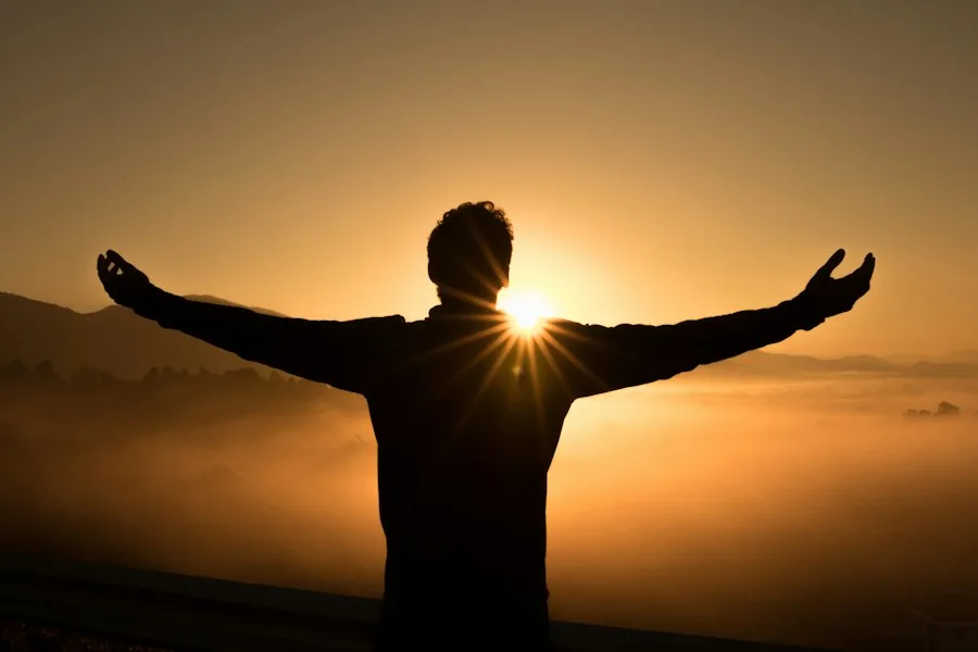 Man with arms outstretched toward a golden sunset (illustrative stock photo)