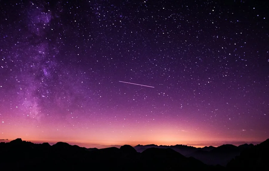Starry night sky glowing purple over a mountain horizon (illustrative stock photo)
