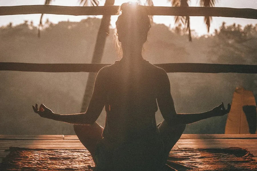 Woman meditating in silhouette on a wooden deck (illustrative stock photo)