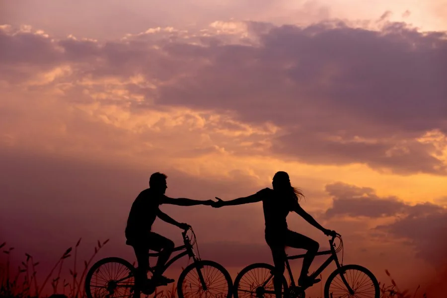 Couple on bicycles reaching for each other's hands at sunset (illustrative stock photo)