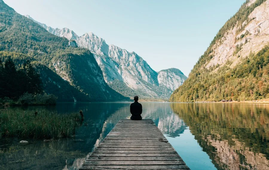 Person sitting on a dock looking across a mountain lake (illustrative stock photo)