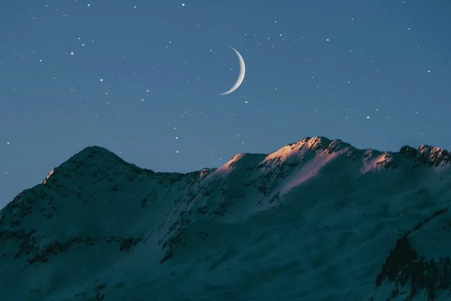 Crescent moon over snowy mountains at dusk (illustrative stock photo)